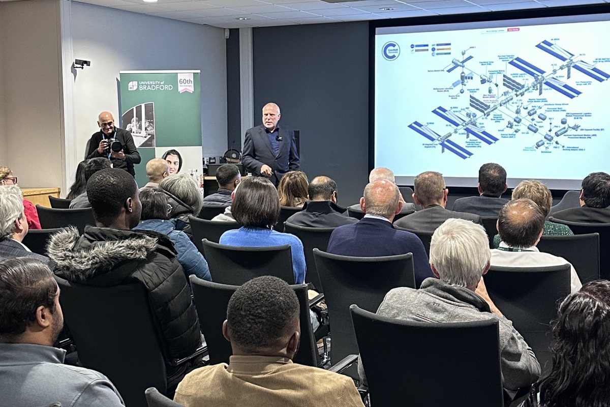 Professor Paul Febvre speaking to a full room in front of a screen showing a diagram of the International Space Station
